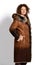 Smiling woman with curly red hair in long brown gradient sheepskin coat with fur collar and cuffs stands in profile