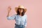Smiling woman with dark hair is getting ready for vacation, waves hand, says hello, happy to see friend, wears straw hat