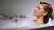 Smiling woman drinking champagne in bath with foam bubbles, evening relax