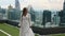 Smiling Woman in Elegant Fashion White Dress Walking on Rooftop with Skyscrapers