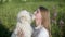 Smiling woman embracing and kissing white dog on green meadow while summer walk. Happy woman dog owner hugging lovely