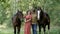 Smiling woman in hat and man with horses in summer forest. Happy couple walking with two horses in green forest at