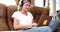 Smiling woman in headphones sits on sofa and watches webinar on laptop