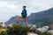 Smiling woman hiker with camera and backpack standing on the top of the mountain. Happy female stepping up on the rock