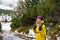 A smiling woman hiker in a yellow down jacket with a backpack wanders the mountain trail in winter.