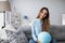 Smiling woman holding globe sitting on the couch at home. Travel planning