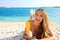 Smiling woman holding sun cream tube protection lying on pebbles beach. Sunscreen girl showing suntan lotion in plastic container