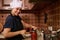 Smiling woman housewife in white chef hat and apron, using seamer, closes lids of jars with freshly canned tomato sauce