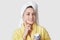 Smiling woman keeps fore finger on face, uses cosmetic cream for staying young and fresh, wears white towel and bathrobe, models