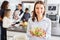 Smiling woman in kitchen with friends holding bowl of fresh lettuce in hands