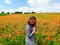 Smiling woman in a long gray dress standing on the red poppy field