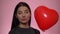 Smiling woman looking at camera, hold red balloon heart. St. Valentine day