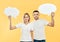 Smiling woman and man holding paper thought bubbles over yellow background