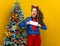 Smiling woman near Christmas tree showing flight tickets