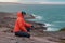 Smiling woman in an orange tourist jacket with a hood on the shore of the cold northern sea