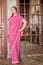 Smiling woman in pink dress stands akimbo in room
