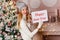 Smiling woman with red lips in a beige sweater and hat holding a sign happy new year. delicate Christmas decor. woman in fluffy