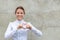 Smiling woman showing heart sign on urban wall background with copy space. Kindness of people concept