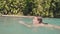 Smiling woman swimming in waterfall lake in tropical rainforest. Cheerful woman enjoying swim in clear water from