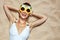 Smiling woman in swimsuit and pineapple glasses laying on sand