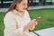 Smiling woman text messaging on smart phone at sunny day. Urban lifestyle concept. Traveler sitting n the bench and