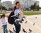 Smiling woman tourist expressing positive emotions while feeding rock pigeons and feral doves in the urban square