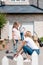 smiling woman tying shoelaces of daughter and man standing behind near cardboard boxes in yard of new