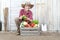 Smiling woman in vegetable garden with wooden box full of vegetables on white wall background with tools