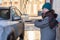 Smiling woman in warm wear washing her suv car at self car-wash station outdoors, using high pressure water jet