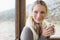 Smiling woman wearing earmuff with cup against window