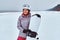 Smiling woman wearing warming sportswear posing with a snowboard on a snowy beach