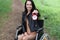 Smiling woman in wheelchair holding alarm clock in park.