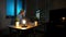 Smiling woman working on computer at night. Smiling female in checkered shirt sitting at lit by small lamp wooden desk