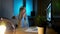 Smiling woman working on computer at night. Smiling female in checkered shirt sitting at lit by small lamp wooden desk