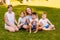 Smiling women and children sit on the green grass. Big happy family, two mothers and three children in white t-shirts. Summer