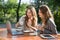 Smiling women sitting outdoors in park drinking coffee using laptop