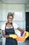 Smiling young african woman holding basket with cleaning equipment at hause