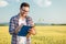 Smiling young agronomist or farmer measuring wheat plant size in a field, writing data into a questionnaire