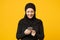 Smiling young arabian muslim woman in hijab black clothes hold in hands cellphone, chatting isolated on yellow wall