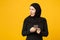 Smiling young arabian muslim woman in hijab black clothes hold in hands cellphone, chatting isolated on yellow wall