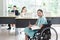 Smiling young Asian woman office worker in wheelchair holding pencil look at camera, disabled people working with colleague