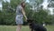 Smiling young attractive woman playing and training the gnintsi shepherd in the park in summer, feeds the dog a banana