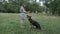 Smiling young attractive woman playing and training the gnintsi shepherd in the park in summer, feeds the dog a banana