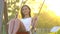 Smiling young beautiful woman swaying on swing in green summer park nature. Pretty girl in white dress swinging at