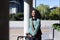 Smiling young biracial businesswoman walking with bicycle on sunny day