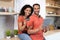 Smiling young black husband and wife show credit card and tablet, enjoy online shopping at kitchen interior