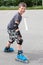 Smiling young boy ready to start riding on roller skates in summer urban park