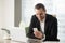 Smiling young businessman in modern office looking at smartphone