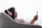 Smiling young calm black woman in wireless headphones typing on smartphone on couch