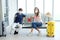 Smiling Young Caucasian couple love is sitting passenger waiting chairs and holding passport for honeymoon trip on vacation